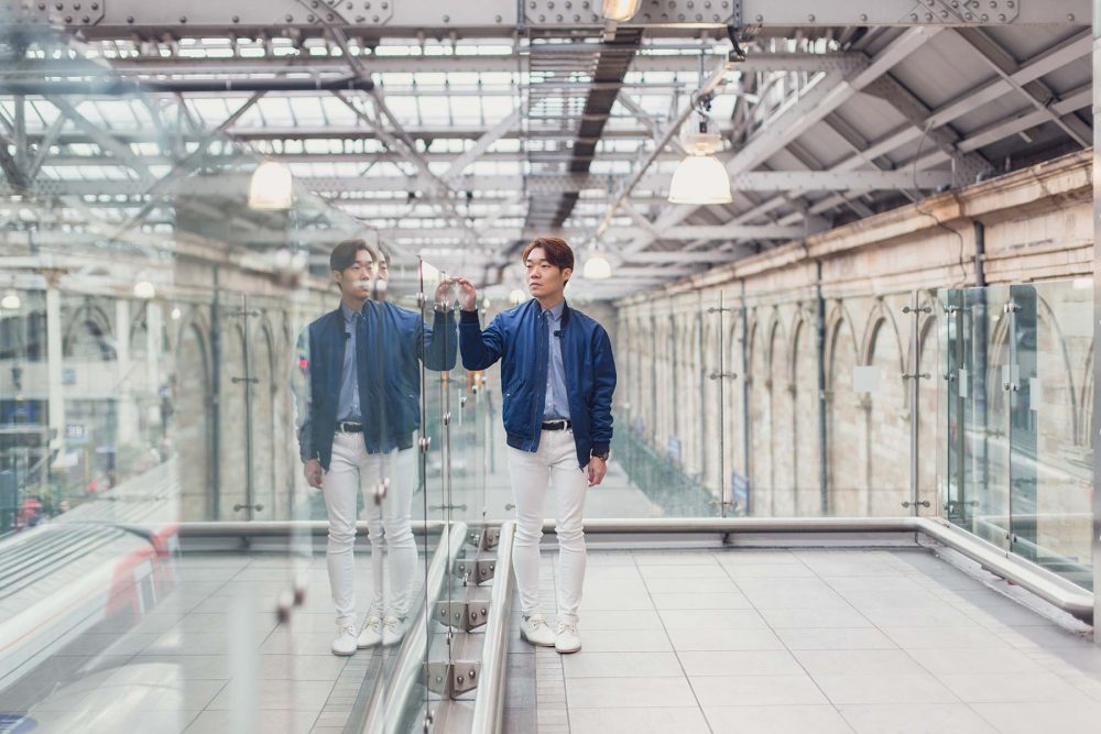 Young asian mal wearing a blue jacket standing inside the Edinburgh Train Station