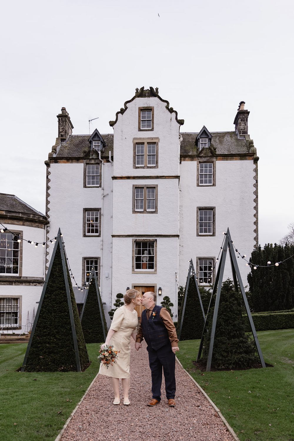 Mature wedding couple kissing in front of Prestonfield house
